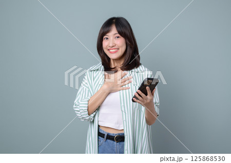 Southeast asian woman smiles happily while holding mobile phone using internet application showing positive emotion and casual style in front of plain background Southeast asian woman smiles happily while holding mobile phone using internet application showing positive emotion and casual style in front of plain background 125868530