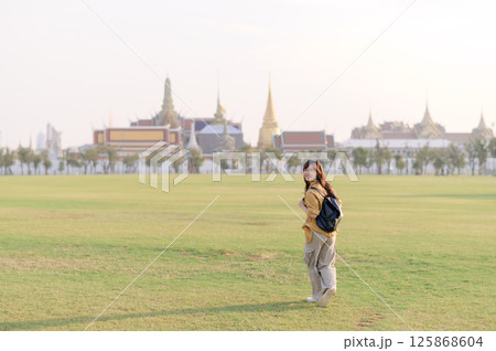 Southeast asian woman enjoys travel concept by exploring vast green field near historic temple complex, smiling happily as she embraces cultural adventure outdoors Southeast asian woman enjoys travel concept by exploring vast green field near historic temple complex, smiling happily as she embraces cultural adventure outdoors 125868604