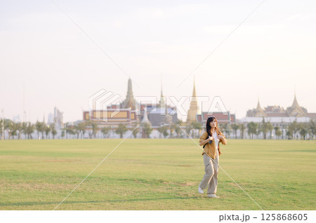 Southeast asian woman enjoys travel concept exploring vast green field with historic temple architecture in background under bright sky creating peaceful and inspiring scene Southeast asian woman enjoys travel concept exploring vast green field with historic temple architecture in background under bright sky creating peaceful and inspiring scene 125868605