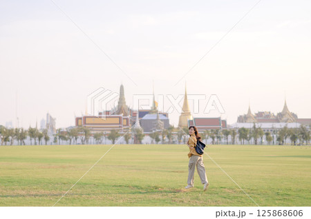 Southeast asian woman enjoys travel concept walking on green grass field with traditional temple and cityscape background in soft light atmosphere Southeast asian woman enjoys travel concept walking on green grass field with traditional temple and cityscape background in soft light atmosphere 125868606