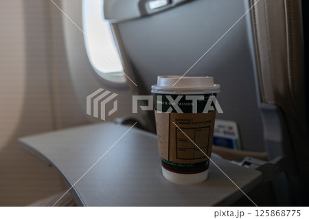 飛行機の座席のテーブルにコーヒーとスマートフォンが置かれている 125868775