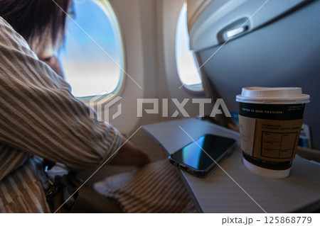 飛行機の座席のテーブルにコーヒーとスマートフォンが置かれている 125868779