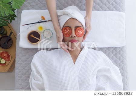Relaxed young asian woman getting eye nature treatment by tomato at spa salon. Wellness and healing concept. Relaxed young asian woman getting eye nature treatment by tomato at spa salon. Wellness and healing concept. 125868922