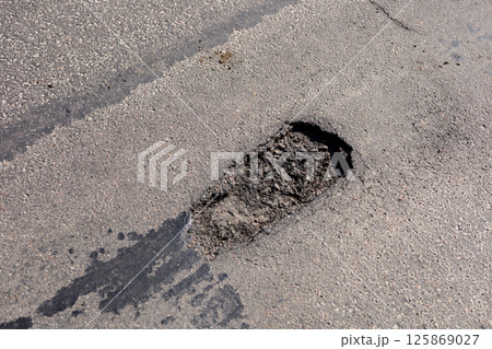 A significant pothole disrupts the smooth surface of a city street, indicating wear from vehicles and weather conditions A significant pothole disrupts the smooth surface of a city street, indicating wear from vehicles and weather conditions 125869027