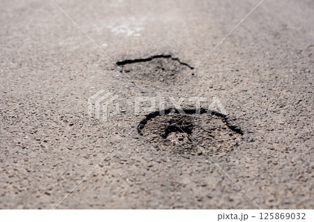 Cracked asphalt sections reveal deterioration of the road, highlighting the need for repairs in an urban area during daylight 125869032