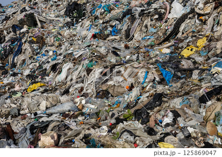 A vast pile of mixed waste is visible, showcasing discarded textiles, plastics, and debris. This landfill reflects ongoing environmental challenges 125869047