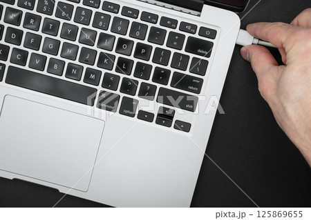 Man hand cord into the computer. Modern laptop computer top view Man hand cord into the computer. Modern laptop computer top view 125869655