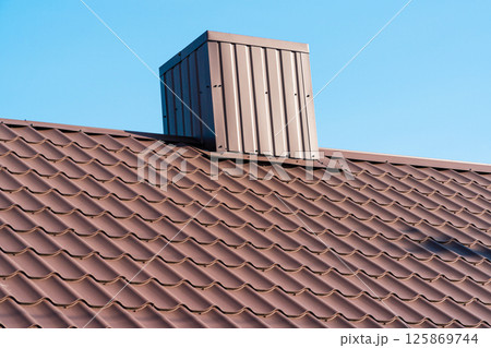 The roof of a house with modern metal tiles and a chimney, against the background of a blue sky. Metal roofing The roof of a house with modern metal tiles and a chimney, against the background of a blue sky. Metal roofing 125869744