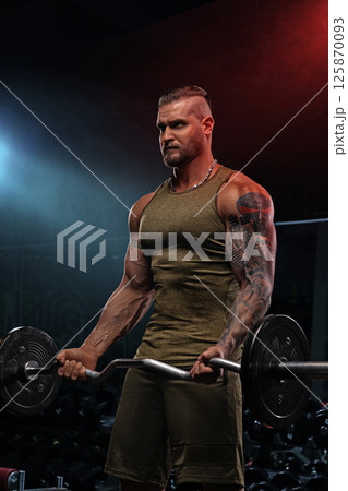 muscular individual is lifting a barbell for bicep curls in a contemporary gym setting. The environment showcases vibrant lighting that highlights the intensity of the workout. 125870093