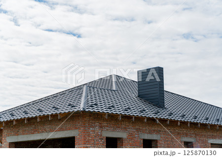 A new brick house with a black roof. Construction of a house. Roof construction 125870130