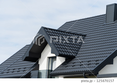 A beautiful modern house is covered with black metal tiles. Roofing of metal profile wavy shape A beautiful modern house is covered with black metal tiles. Roofing of metal profile wavy shape 125870157