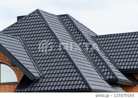 Black metal profile roof installed on a modern house. Modern types of roofing materials. Modern construction Black metal profile roof installed on a modern house. Modern types of roofing materials. Modern construction 125870165