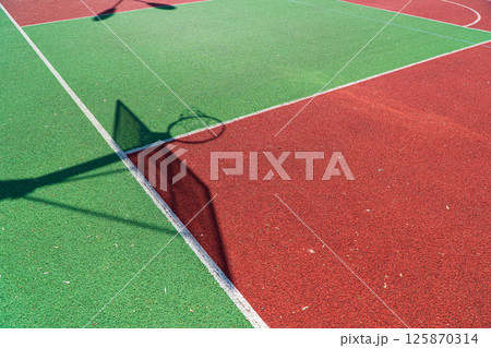 Shadow of the rack with shield and basketball ring on basketball field. Colorful basketball lines on an outdoor court Shadow of the rack with shield and basketball ring on basketball field. Colorful basketball lines on an outdoor court 125870314