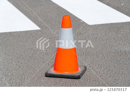Traffic cone, with white and orange stripes on gray asphalt. Construction cone. Symbol of restrictions, roadworks, attention Traffic cone, with white and orange stripes on gray asphalt. Construction cone. Symbol of restrictions, roadworks, attention 125870317