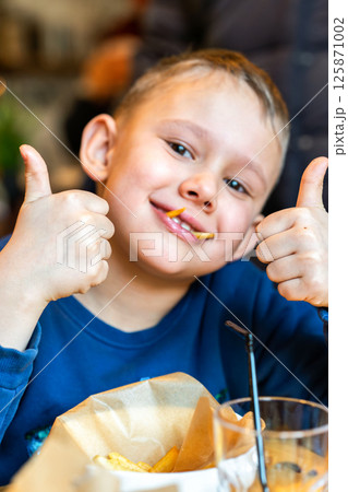 Smiling boy showing thumbs up with fries in mouth, concept of childhood joy and fun eating Smiling boy showing thumbs up with fries in mouth, concept of childhood joy and fun eating 125871002