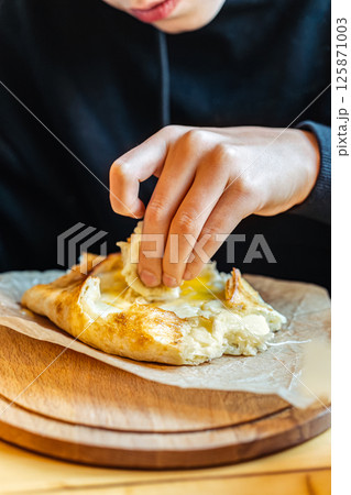 Boy tearing off cheesy bread from khachapuri with egg, close-up view, concept of traditional Georgian cuisine 125871003