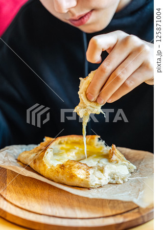 Boy tearing off cheesy bread from khachapuri with egg, close-up view, concept of traditional Georgian cuisine 125871004