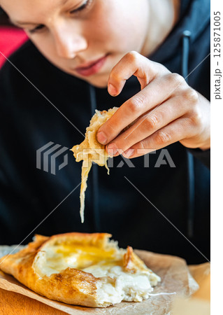 Boy tearing off cheesy bread from khachapuri with egg, close-up view, concept of traditional Georgian cuisine Boy tearing off cheesy bread from khachapuri with egg, close-up view, concept of traditional Georgian cuisine 125871005