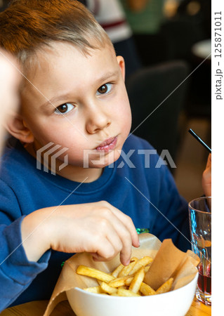 Young boy is eating French fries and drinking soda at a restaurant table indoors close-up, concept of casual dining fun 125871011