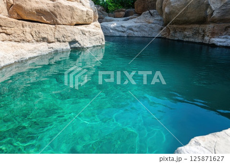 Natural rock pool with crystal clear turquoise water surrounded by large stone formations in a serene outdoor tropical setting 125871627
