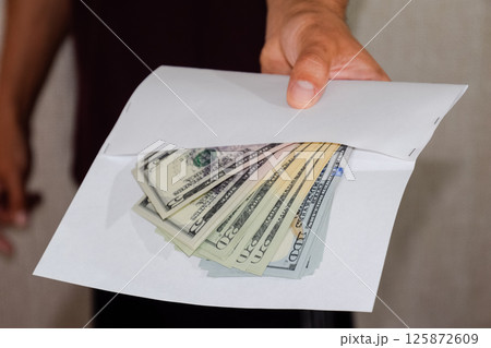 Money in white envelope in the hands of a man. Dollars, a wad of dollars. 125872609