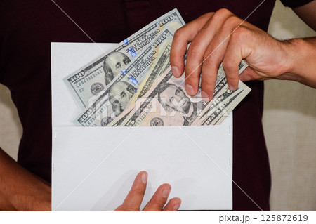 Money in white envelope in the hands of a man. Dollars, a wad of dollars. 125872619