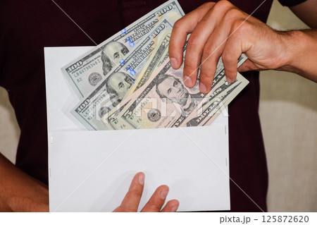 Money in white envelope in the hands of a man. Dollars, a wad of dollars. 125872620