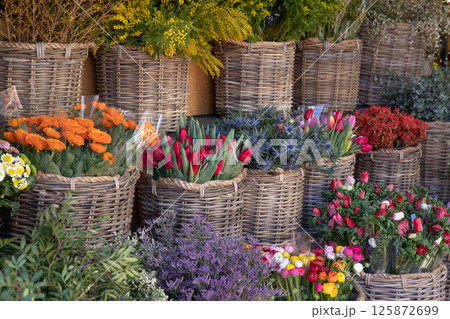 A vibrant assortment of flowers arranged in woven baskets at a market. Brightly colored blooms like tulips, roses, and daisies bring life to the outdoor space, highlighting the beauty of nature. A vibrant assortment of flowers arranged in woven baskets at a market. Brightly colored blooms like tulips, roses, and daisies bring life to the outdoor space, highlighting the beauty of nature. 125872699