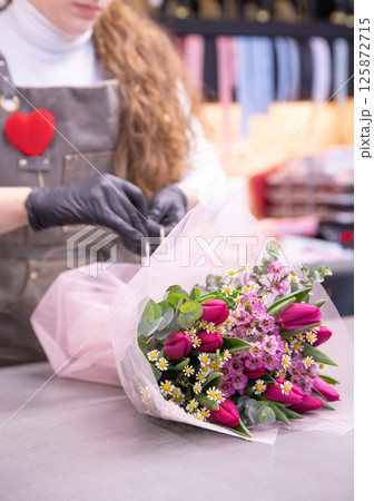 Florist packs beautiful flower arrangement of pink tulips, wax flower, chamomile, eucalyptus - stylish gift for Valentine's Day. Vertical. Close-up. 125872715