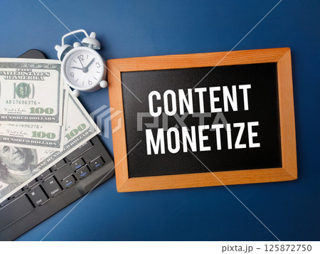 Top view wooden board and banknotes with the word CONTENT MONETIZE on a blue background. Top view wooden board and banknotes with the word CONTENT MONETIZE on a blue background. 125872750