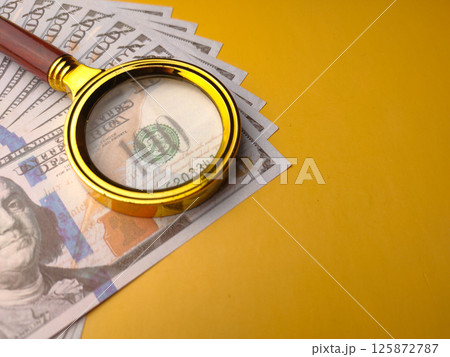 Closeup gold magnifying glass and one hundred dollars on a yellow background. 125872787