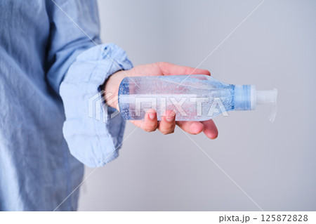 An unrecognizable person in blue clothes holds a bottle of hyaluronic micellar gel for washing. 125872828