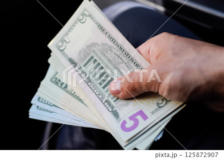 man hands over money in a car. A wad of dollars in his hand. man hands over money in a car. A wad of dollars in his hand. 125872907