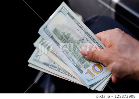 man hands over money in a car. A wad of dollars in his hand. 125872909
