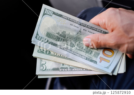 man hands over money in a car. A wad of dollars in his hand. man hands over money in a car. A wad of dollars in his hand. 125872910