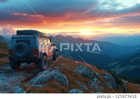 Rugged 4x4 stands on a high ridge at dawn, golden sun rising over vast peaks in a bold and wild overland escape 125873418