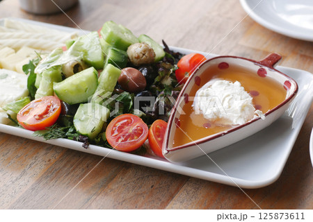 Fresh salad platter with olives, tomatoes, and honey dip is served 125873611