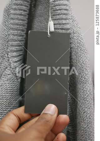 Gray sweater with an attached price tag being held up by a hand Gray sweater with an attached price tag being held up by a hand 125873688
