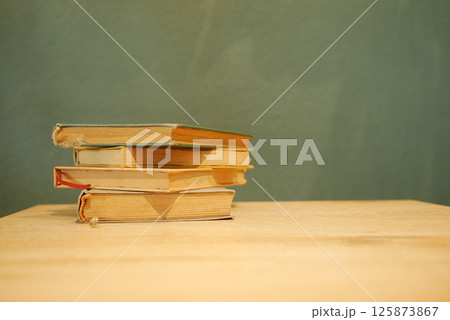 Stacked books on a wooden table against a textured wall Stacked books on a wooden table against a textured wall 125873867