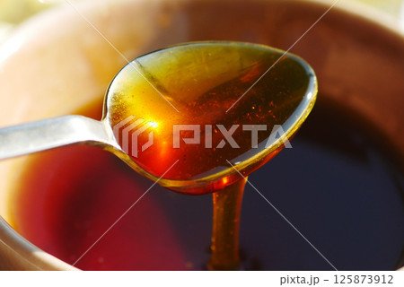 Golden honey dripping from a spoon in natural light 125873912