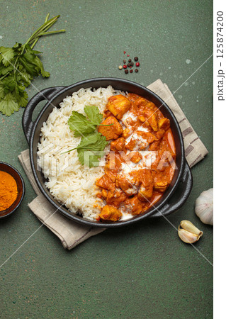 Indian dish chicken tikka masala served with rice and spices on green background top view Indian dish chicken tikka masala served with rice and spices on green background top view 125874200