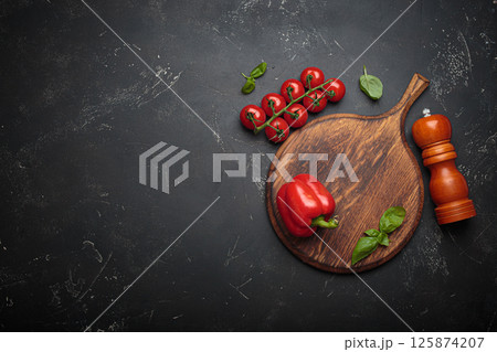 Food background with fresh vegetables and pepper mill resting on rustic wooden cutting board, black background, space for text Food background with fresh vegetables and pepper mill resting on rustic wooden cutting board, black background, space for text 125874207