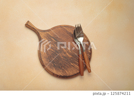 Empty round wooden empty chopping board with cutlery on beige textured background, space for text top view 125874211