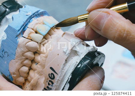 A close-up view of a dental technician holding a toothbrush for prosthesis manufacturing, showcasing hands and tools. 125874411
