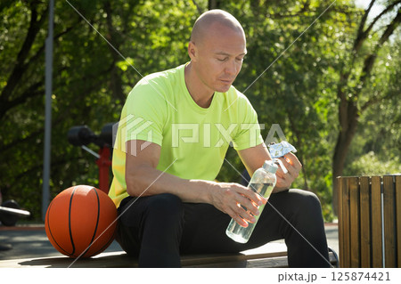 Basketball player eating energy bar or protein bar and drinking water while resting after training at stadium. Healthy protein sugar free snack dieting food for sporty lifestyle. Basketball player eating energy bar or protein bar and drinking water while resting after training at stadium. Healthy protein sugar free snack dieting food for sporty lifestyle. 125874421