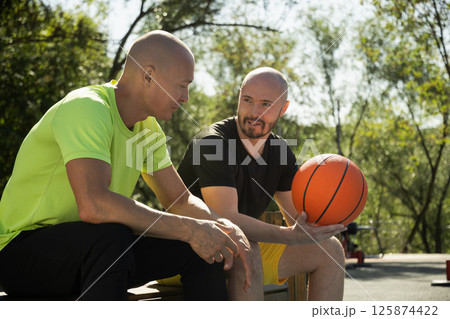 Two basketball players sitting on bench and discussing game on sports court. Sports competition game. Outdoor workout. Team sport. 125874422