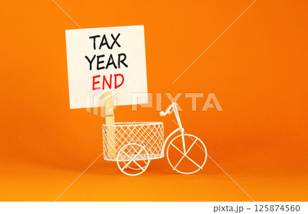 Tax year end symbol. Concept words Tax year end on beautiful white paper on clothespin. Beautiful orange background. Miniature white bicycle. Business tax year end concept. Copy space. Tax year end symbol. Concept words Tax year end on beautiful white paper on clothespin. Beautiful orange background. Miniature white bicycle. Business tax year end concept. Copy space. 125874560