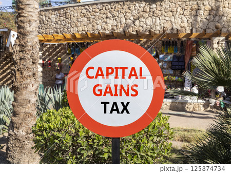 Capital gains tax symbol. Concept words Capital gains tax on beautiful big white road sign. Beautiful palm tree hotel market background. Business and capital gains tax concept. Copy space. 125874734