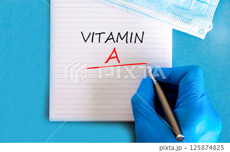 Vitamin A symbol. Concept words Vitamin A on beautiful white note. Doctor's hand in blue medical glove. Medical mask. Beautiful blue background. Medical healthy lifestyle Vitamin A concept. Vitamin A symbol. Concept words Vitamin A on beautiful white note. Doctor's hand in blue medical glove. Medical mask. Beautiful blue background. Medical healthy lifestyle Vitamin A concept. 125874825