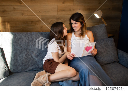 Preteen girl surprising mom for mother's day with greeting card. Happy mother's day concept. 125874934